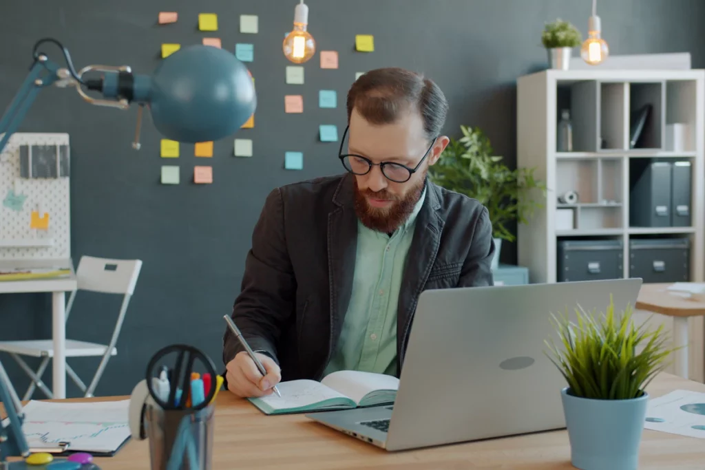 Dirigeant qui s'organise au travail en notant ses priorités dans un carnet à son bureau